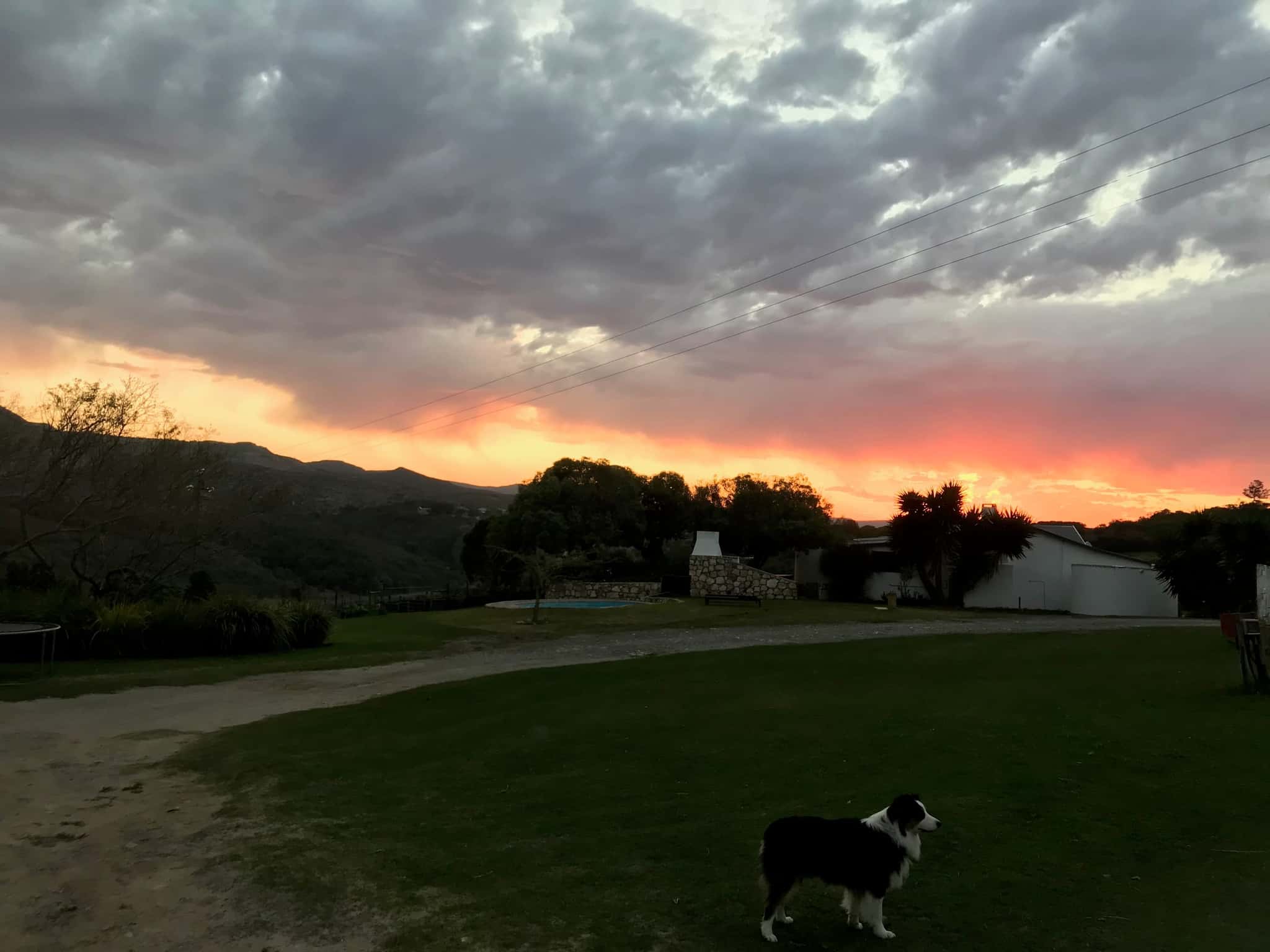 A fiery sunset over the farm lawn and cottages, the hills dark against the sky.