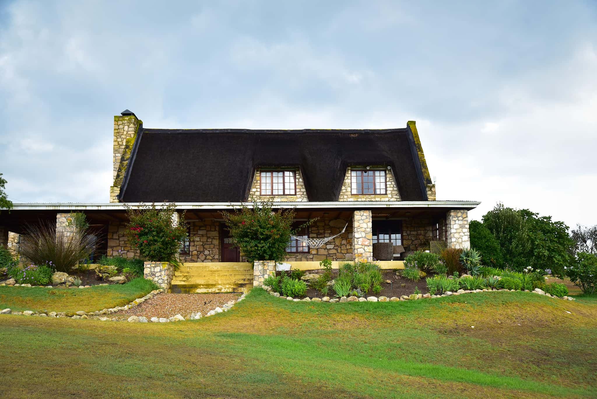 The thatched front of Stonehouse Lodge with its stone chimney, wrap-around veranda and flowering garden.