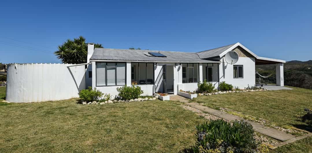 White House Cottage, the 1920 farmhouse: a single-storey white house with a grey roof and a lawn in front.