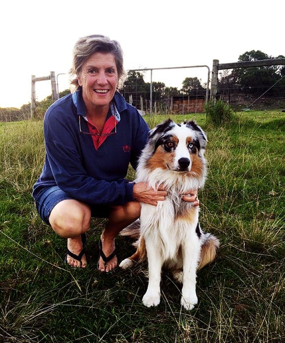 Alison Bryant crouching in the grass with her Australian shepherd.