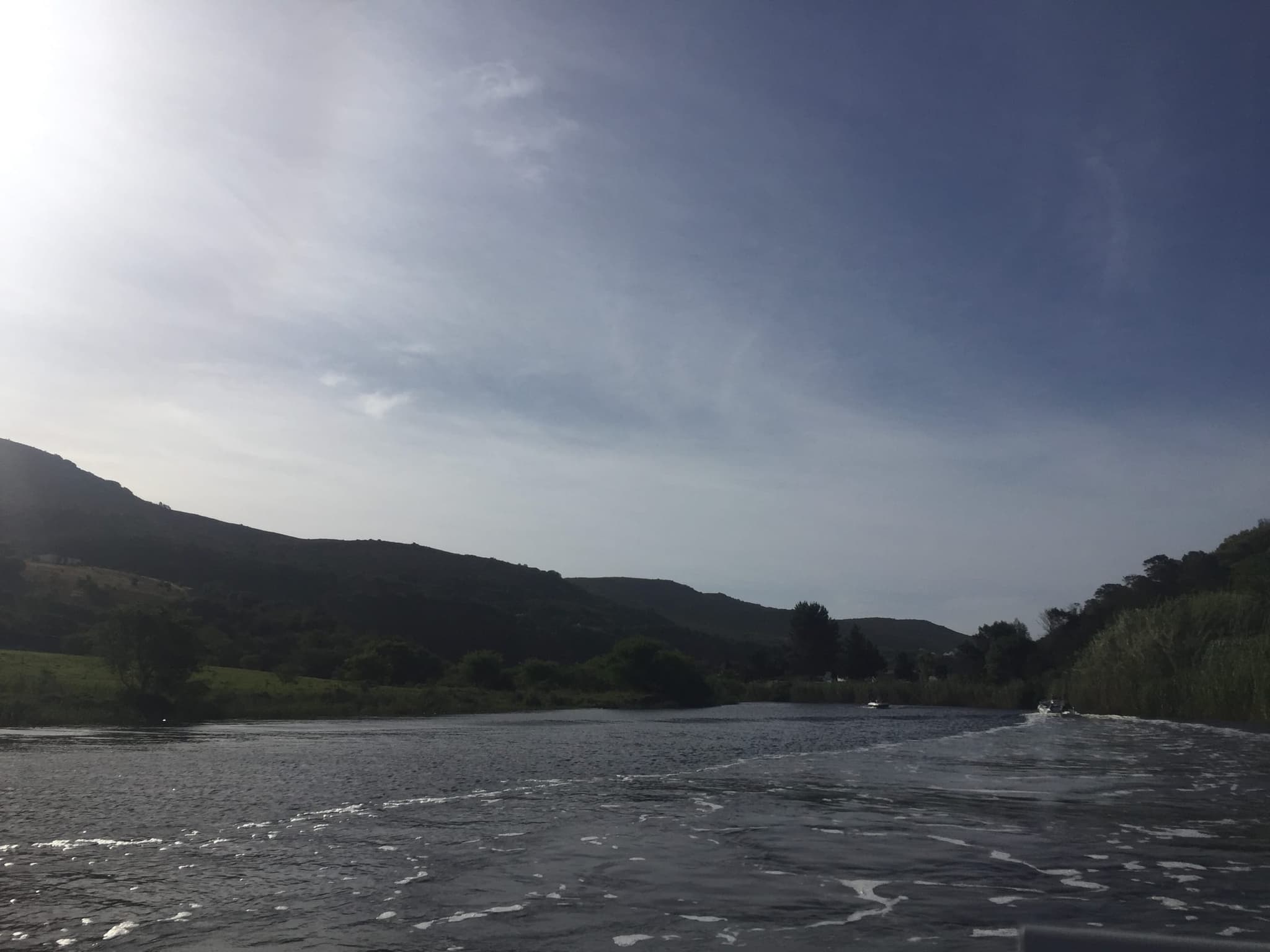 The Goukou River and its hills seen from a boat, the water silver under the clouds.