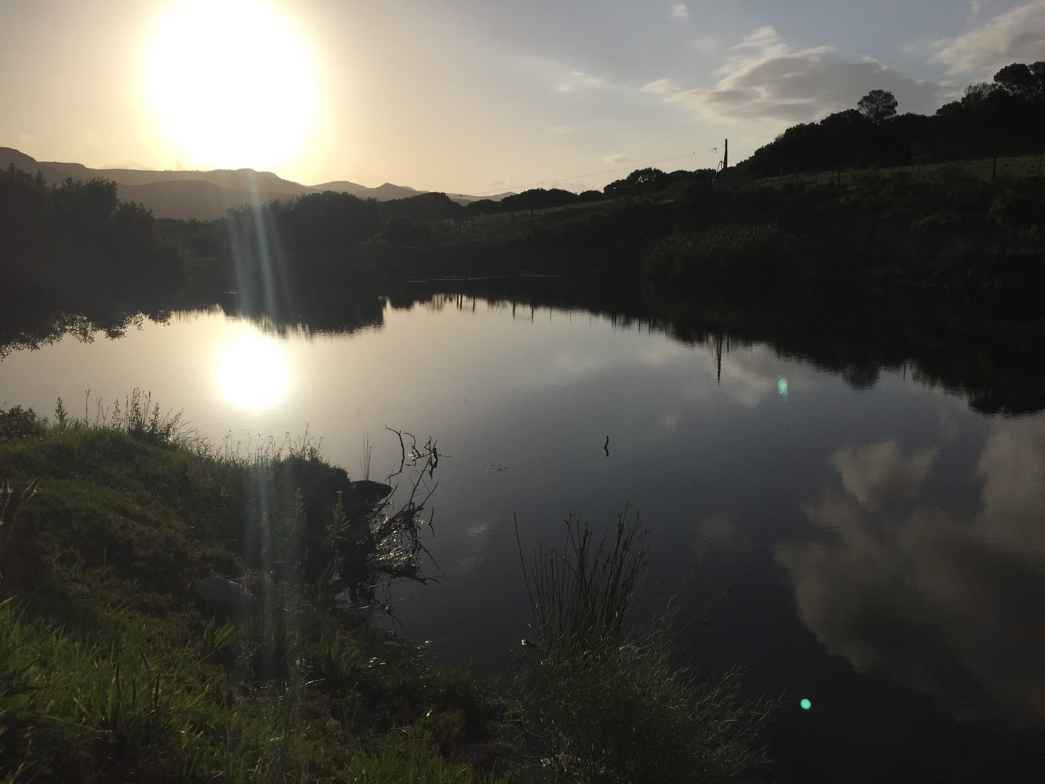 Low sun over the Goukou in the evening, the wooded far bank in silhouette and its reflection on the water.