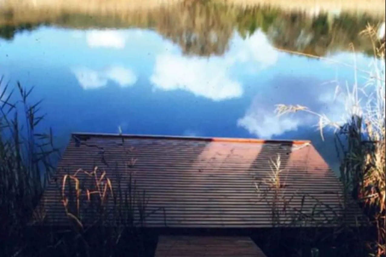 The wooden jetty on the water, with clouds and blue sky reflected around it.