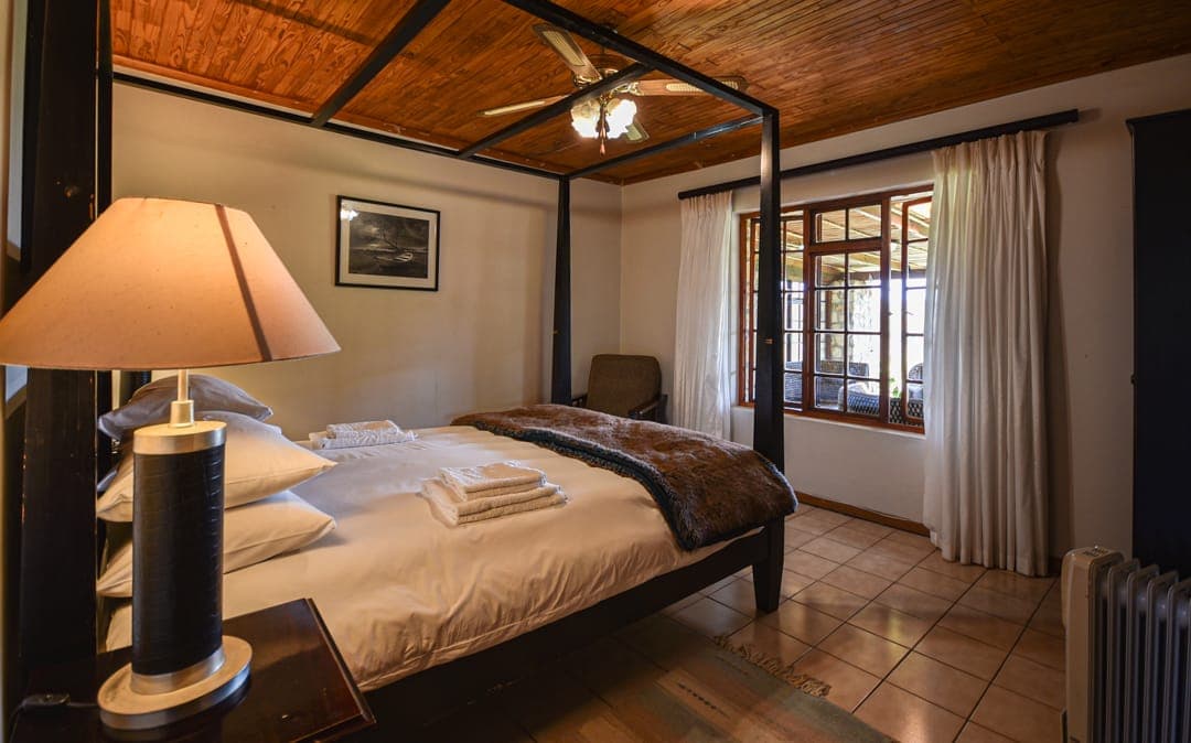 A four-poster bed under the thatch ceiling at Stonehouse Lodge, with towels folded on the bed and windows onto the farm.