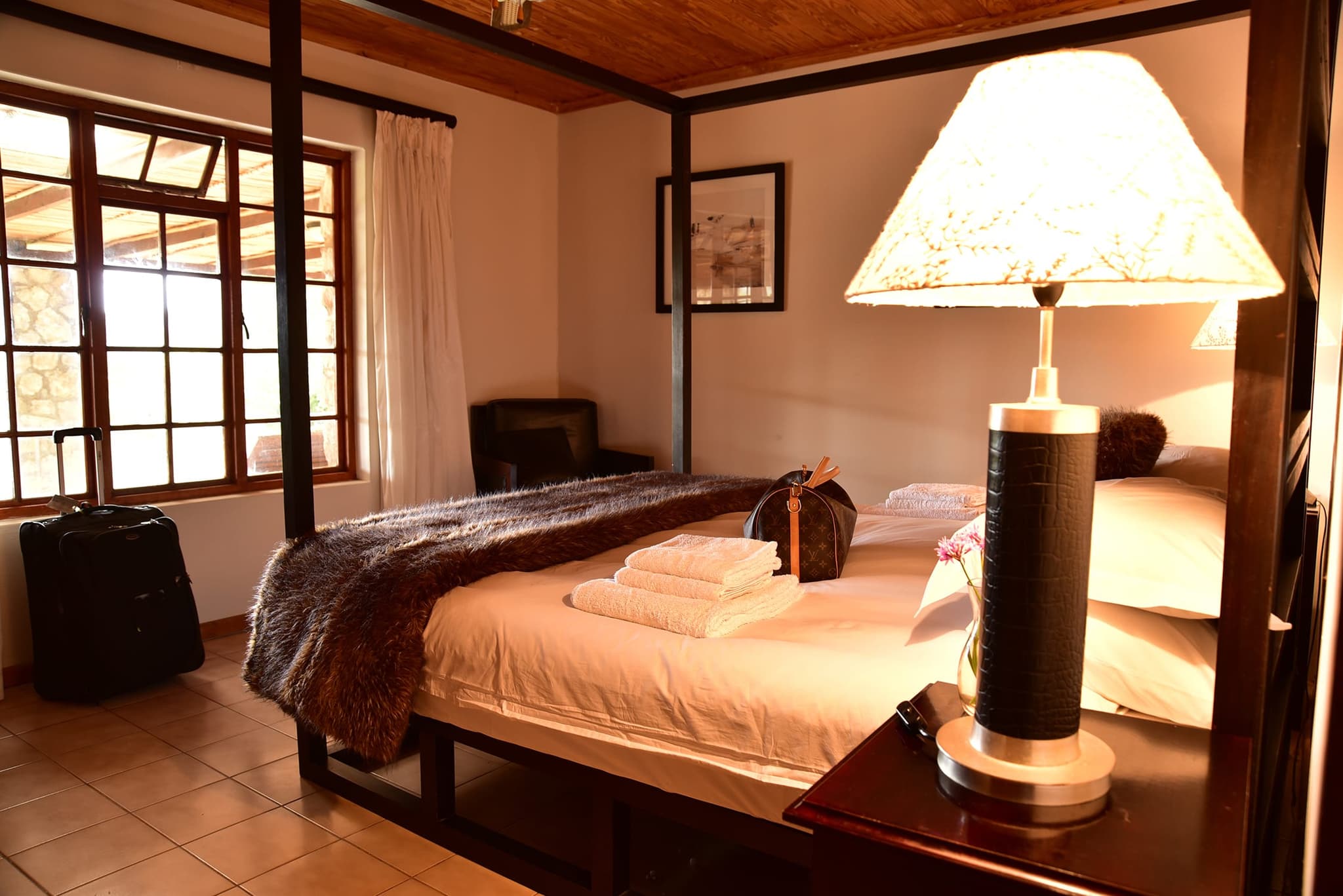 A bedroom at Stonehouse Lodge with a wooden four-poster bed, folded towels, a reading lamp and windows onto the veranda.