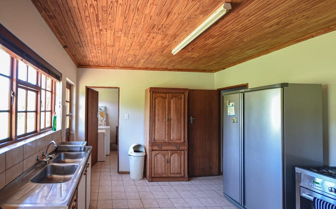 The Stonehouse kitchen with a wooden ceiling, double sink, tall fridge and a pantry cupboard.