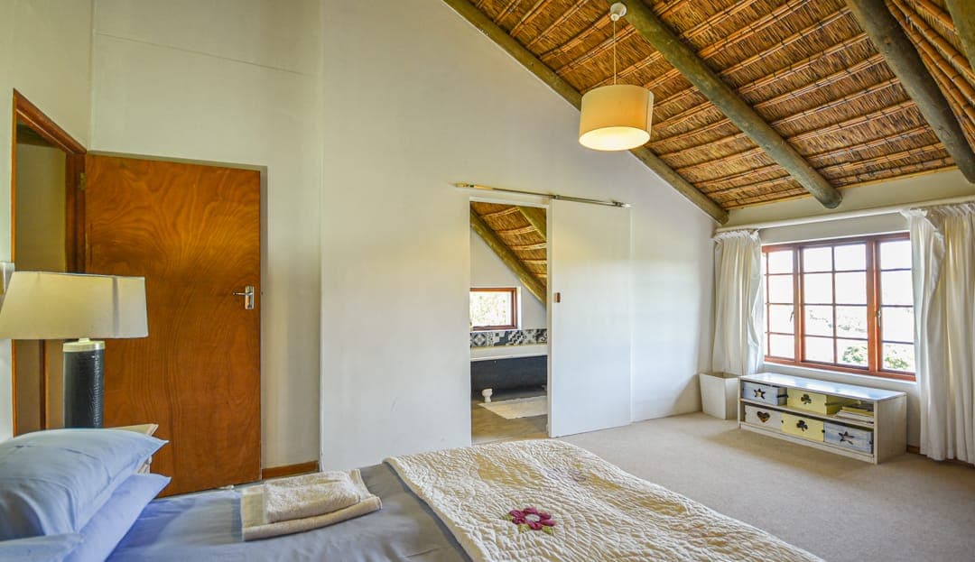 A loft bedroom under the sloping thatch at Stonehouse Lodge, with a window seat at the far end.