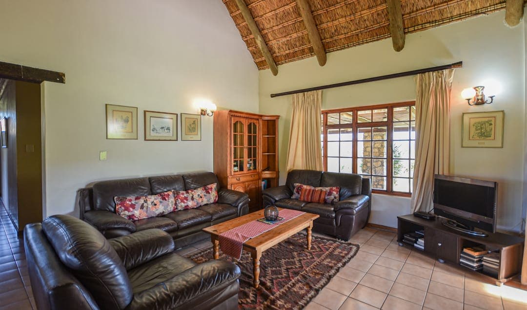 The Stonehouse lounge under a thatch and pole ceiling, with leather sofas, a TV and windows onto the garden.
