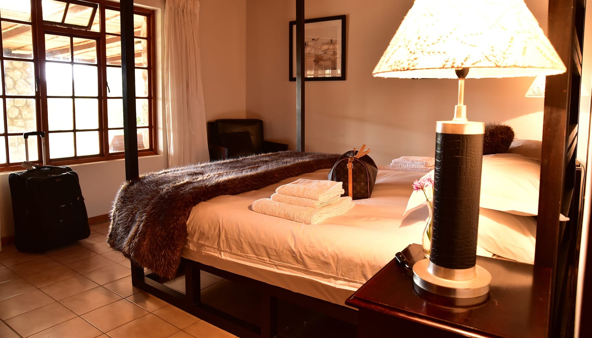 The king-size four-poster master bedroom at Stonehouse Lodge, with a bedside lamp and terracotta floor.