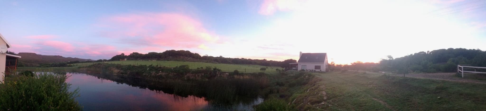 A panorama of the farm wetland at dusk under a pink sky, the white cottage at the edge.