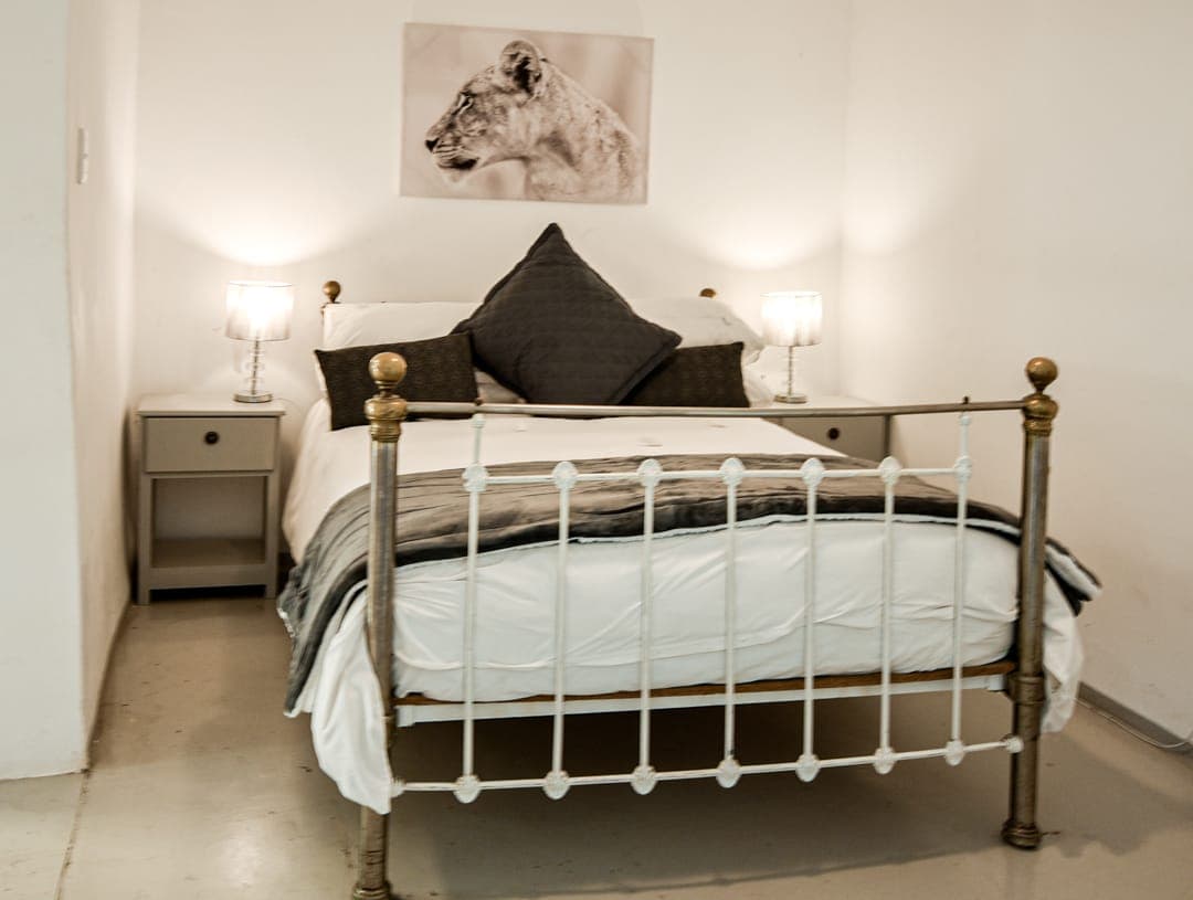 A brass-and-iron double bed with grey linen and bedside lamps at White House Cottage.