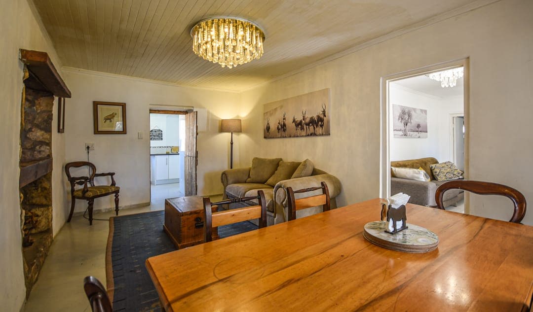 The wooden dining table at White House Cottage, with the lounge and an open door through to a bedroom.