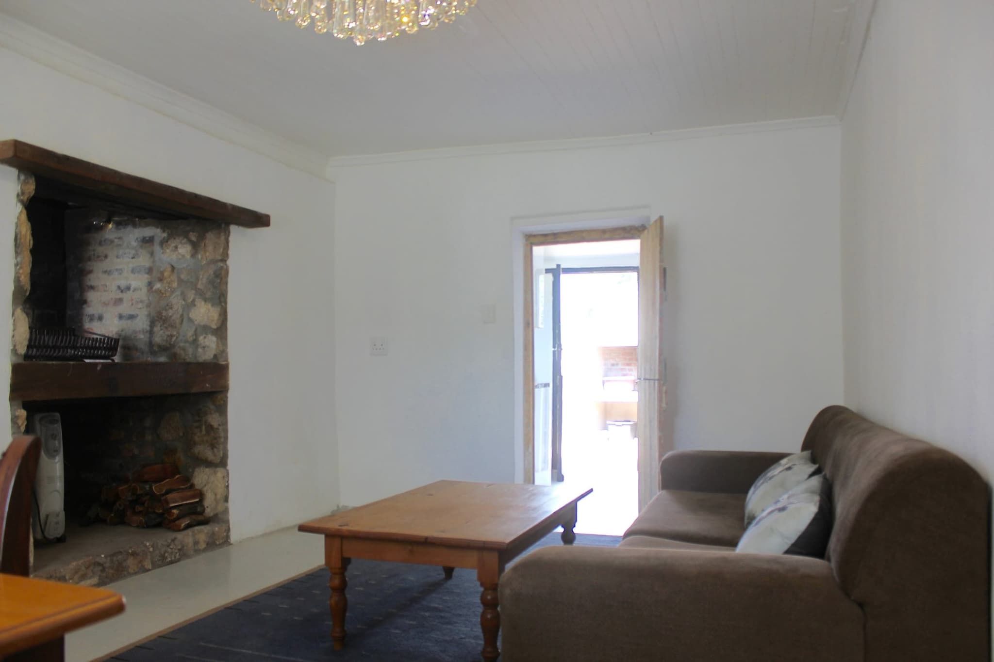 The indoor braai in the stone fireplace of White House Cottage, with the lounge sofa and a door out to the garden.