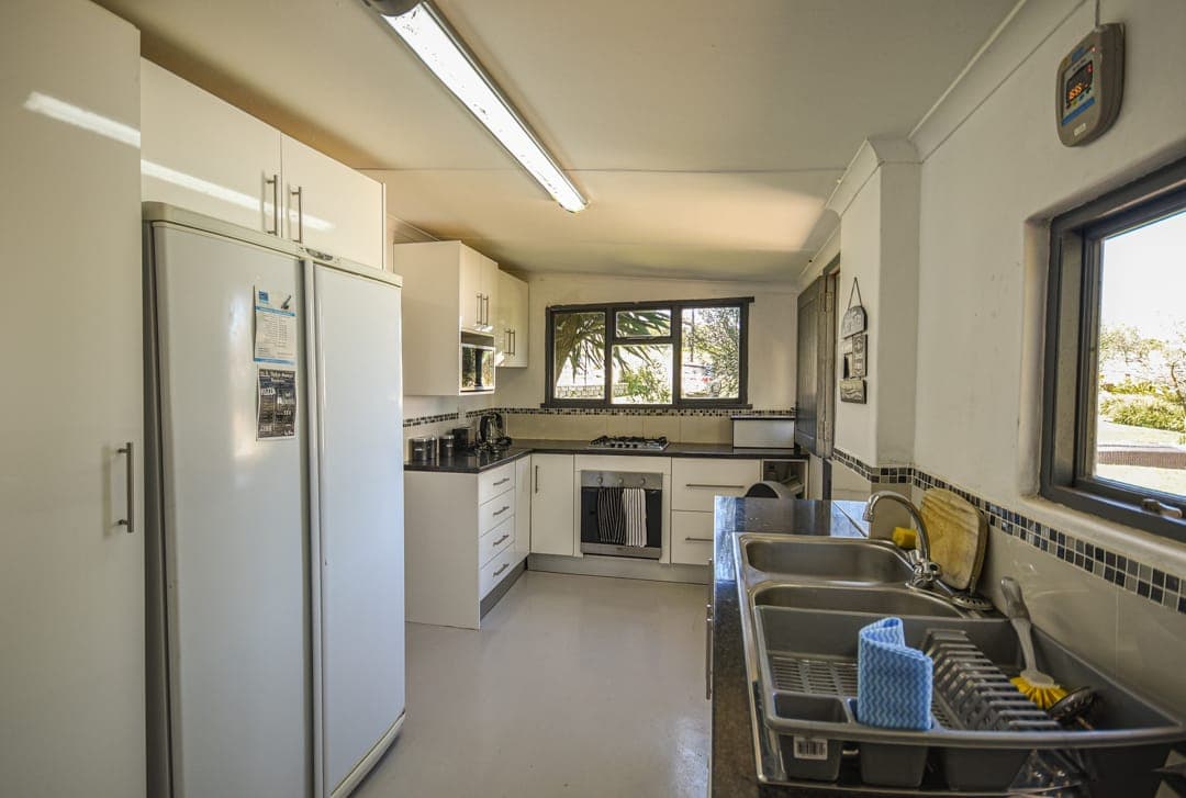 The full White House Cottage kitchen: double-door fridge, white cupboards, dark counters and a window over the garden.