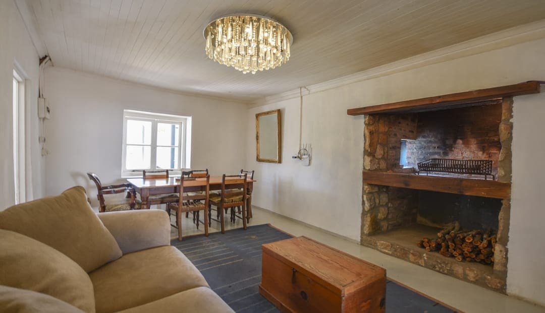 The White House Cottage lounge: a stone hearth stacked with wood, a chandelier and the dining table beyond.