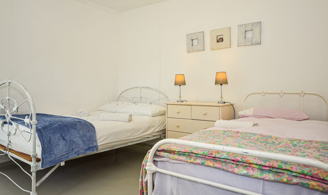 Two white iron single beds and a chest of drawers in the White House Cottage family room.