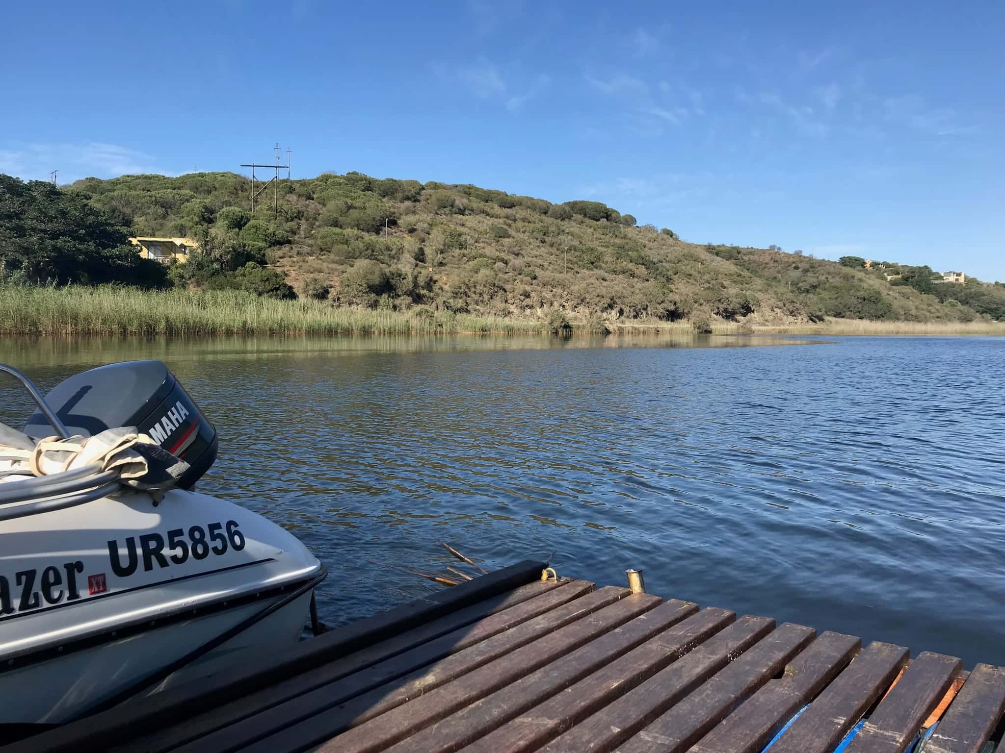 The Goukou River from the farm jetty: a boat moored alongside, blue water and wooded hills.