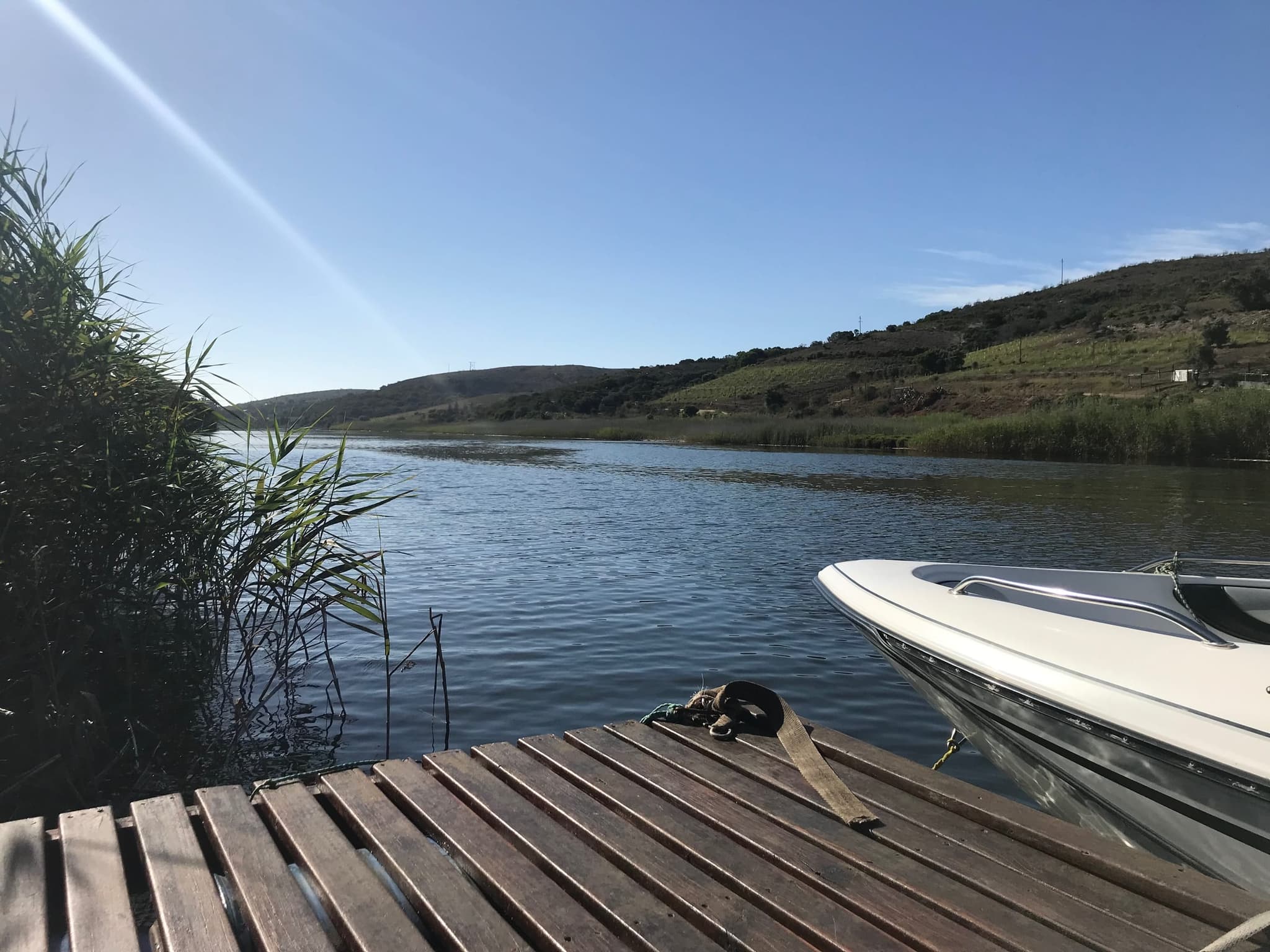 The farm jetty on the Goukou River with a speedboat tied up and reeds on the bank.